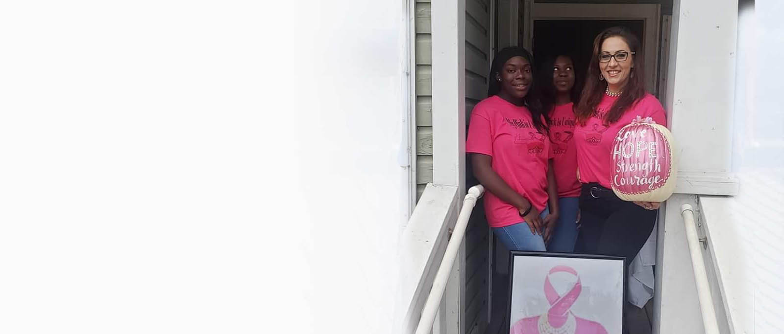 Three women in pink shirts holding pink pumpkin